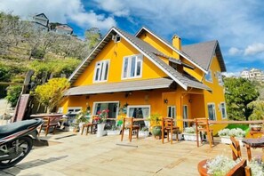 A yellow house with a tiled patio, outdoor furniture, and a motorcycle parked in front. - Michelia Valley Hotel (Dalat)