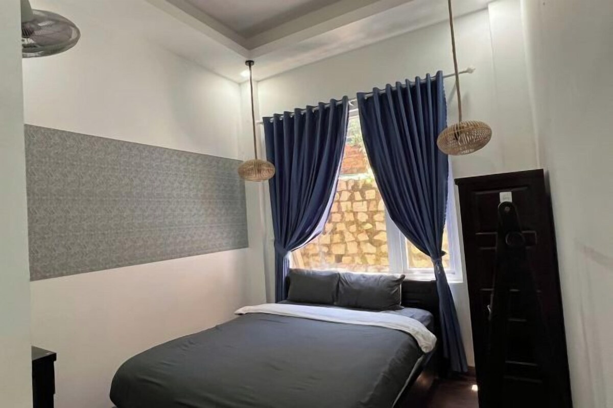 Een slaapkamer met een bed, een raam met gordijnen, een wandlamp en een deur.
