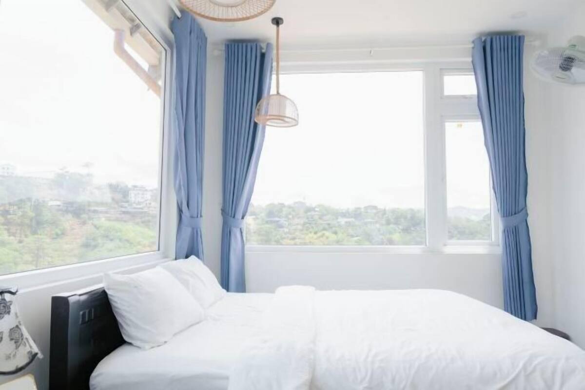 A hotel room with a bed, curtains, a window, and a hanging light fixture.