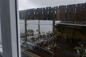 A view of a covered outdoor seating area with tables and chairs, a wooden fence, and potted plants. - Michelia Valley Hotel (Dalat)