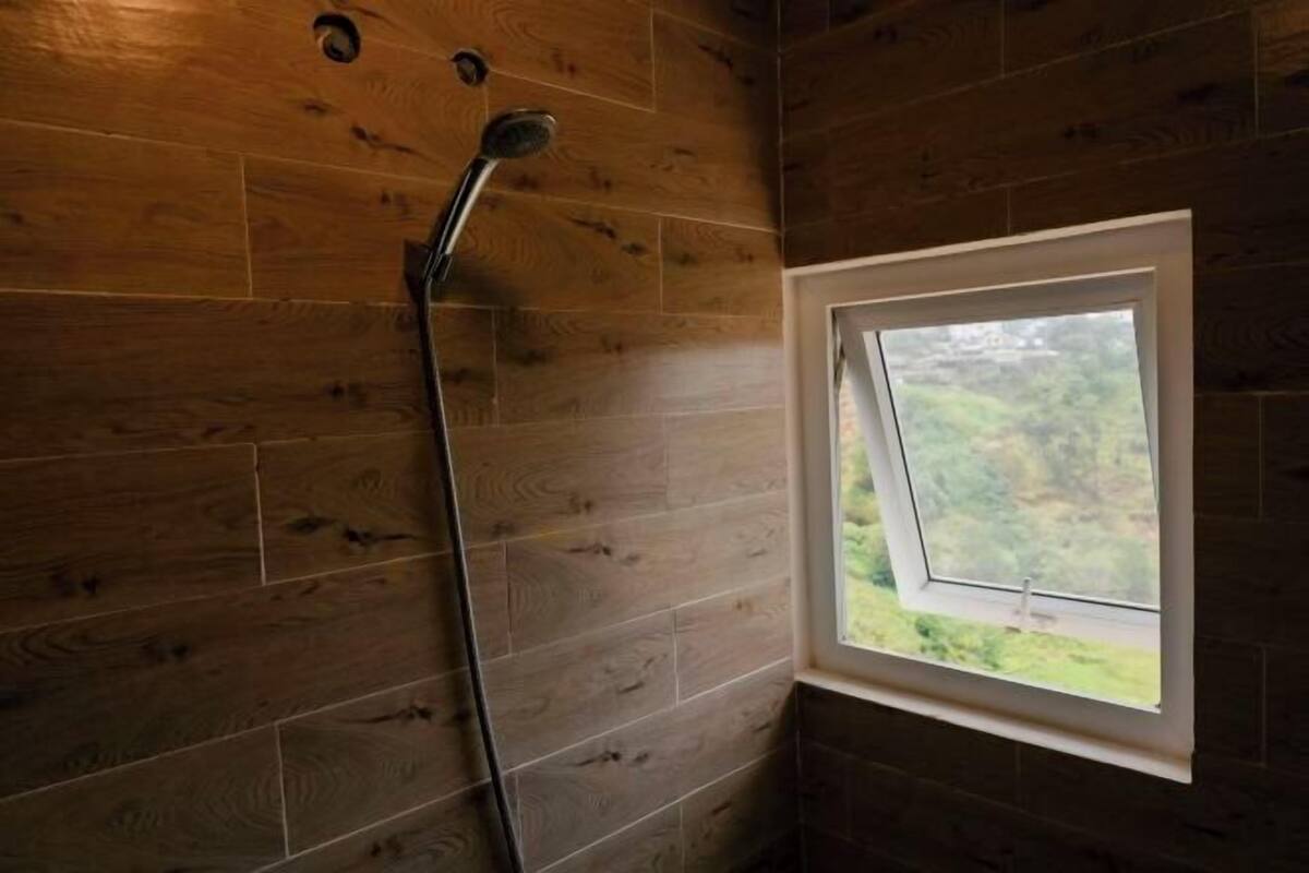 A bathroom with wooden walls, a shower, and a window with a view.