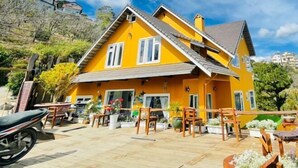 A yellow house with a tiled patio, wooden furniture, and potted plants. - Michelia Valley Hotel (Dalat)