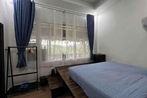 Ein Schlafzimmer mit einem Bett, einem Fenster mit Vorhängen, einem Nachttisch und einem kleinen Tisch.