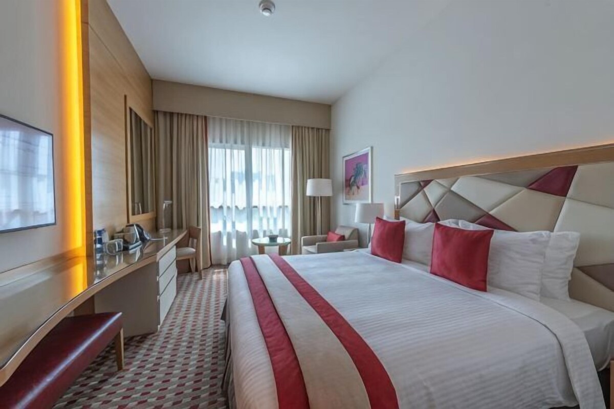 A hotel room with a large bed, a desk, a chair, a TV, and a window with curtains.