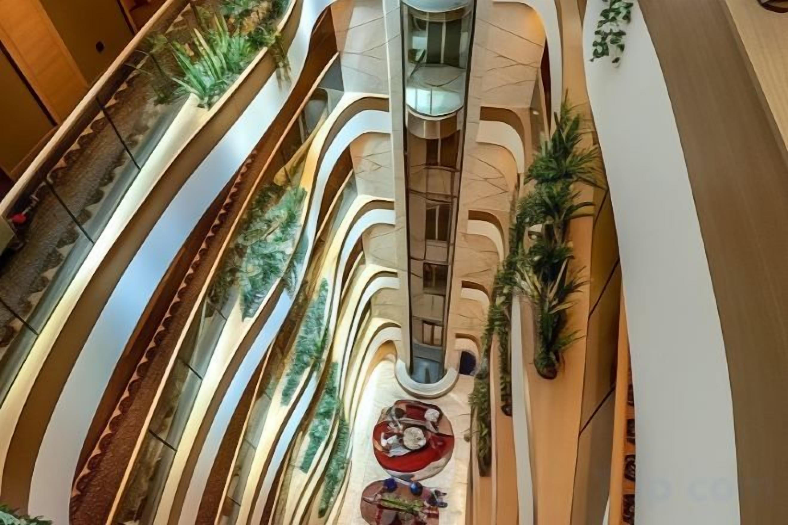 A multi-level atrium with curved balconies, indoor plants, and a central spiral staircase.