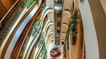 A multi-level atrium with curved balconies, indoor plants, and a central spiral staircase.
