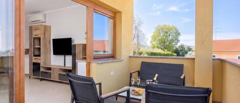 A balcony with two chairs, a table, and a TV in the background.