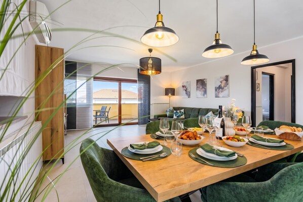 A modern dining area with a wooden table set for a meal, green upholstered chairs, and pendant lighting.