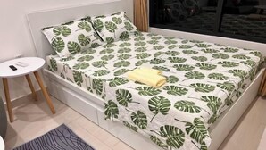 A bed with a leaf-patterned bedspread, a bedside table, a small rug, and slippers. - Vinhone Grand Park Homestay - ZEN Garden Residence (Ho Chi Minh City)
