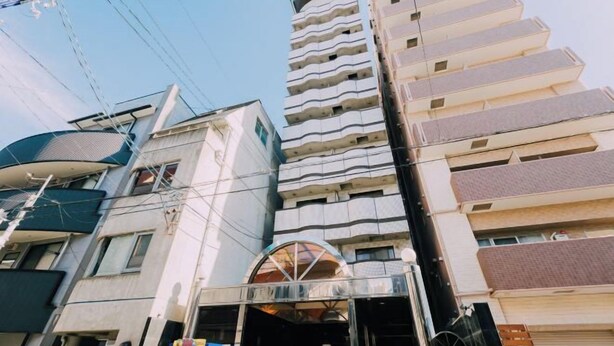 A multi-story building with a prominent entrance featuring a glass canopy. - Nippombashi Back Kuromon AFP Apartment (Osaka)
