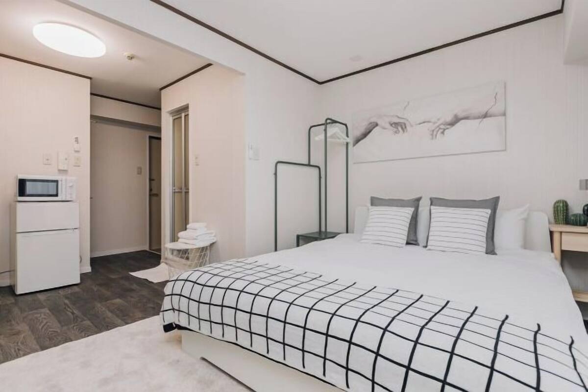 A modern hotel room with a large bed, a bedside table, a mirror, and a wall-mounted artwork.