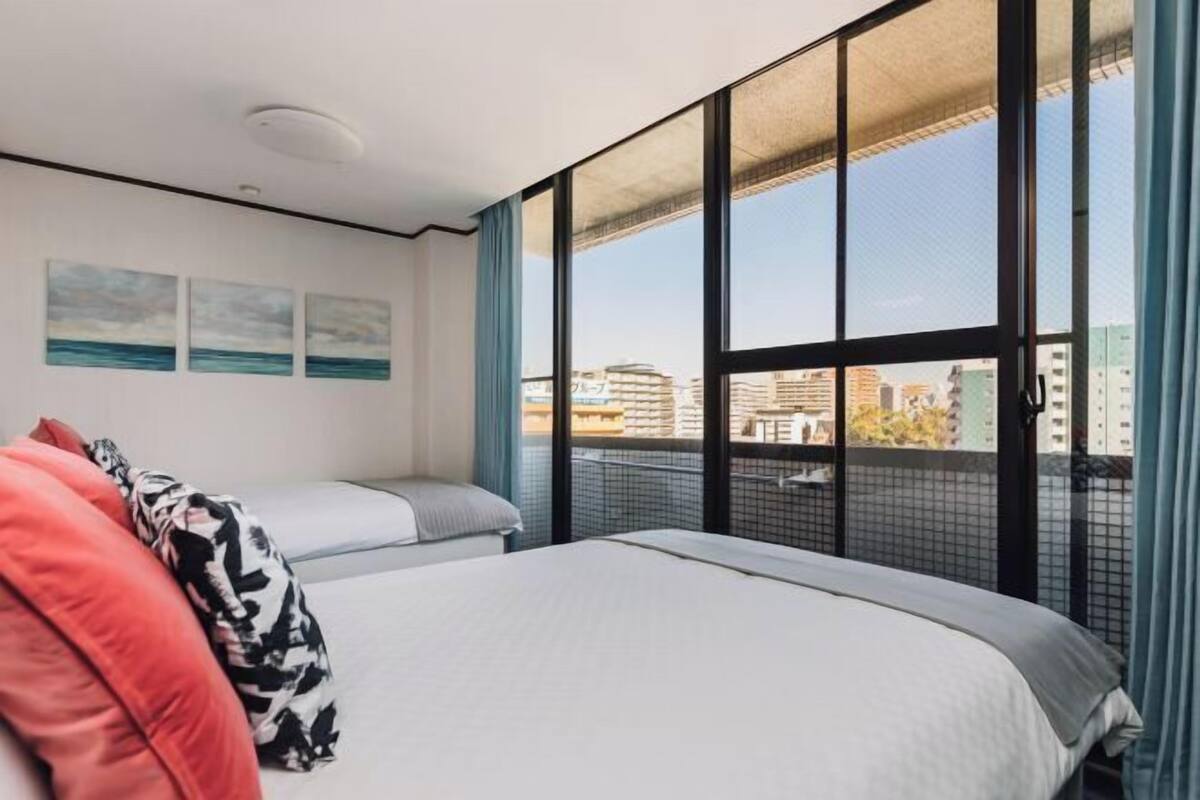 A hotel room with a large window, a bed, a bedside table, and a view of the cityscape.