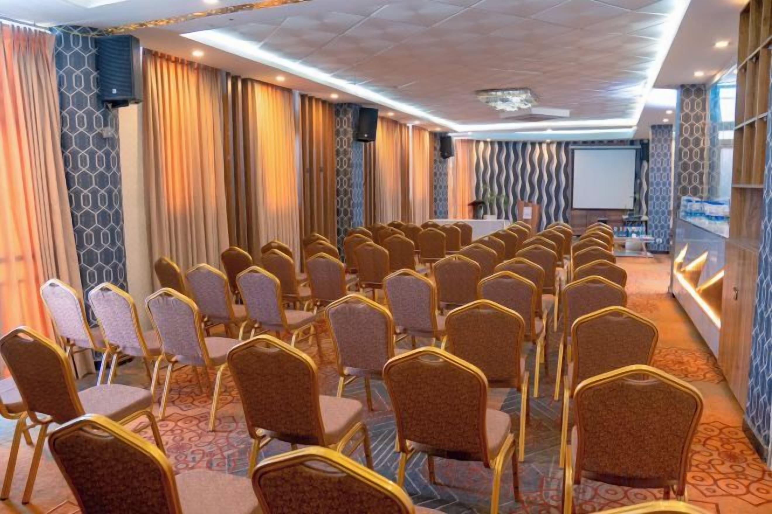 A conference room with rows of chairs, a podium, and a projection screen.