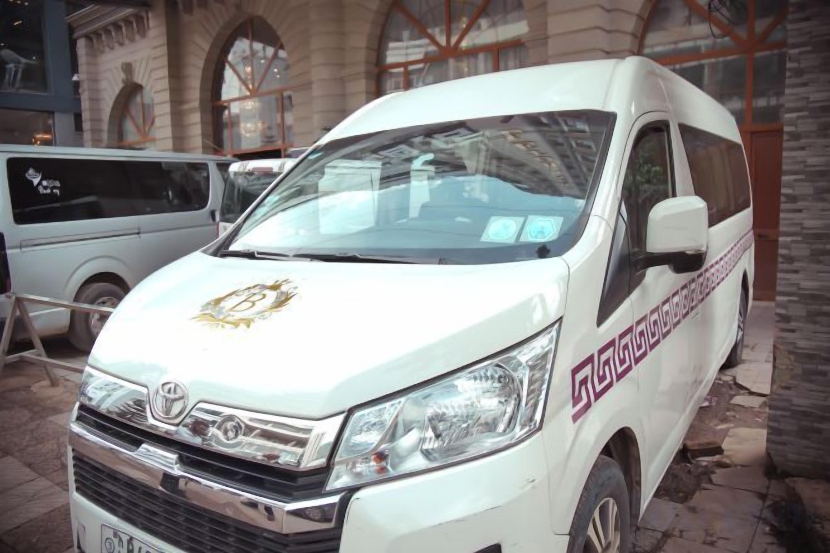 A white van with a logo on the front, parked in front of a building with arched windows.