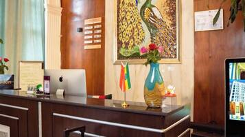 A reception desk with a computer, a vase with flowers, and a peacock painting on the wall.