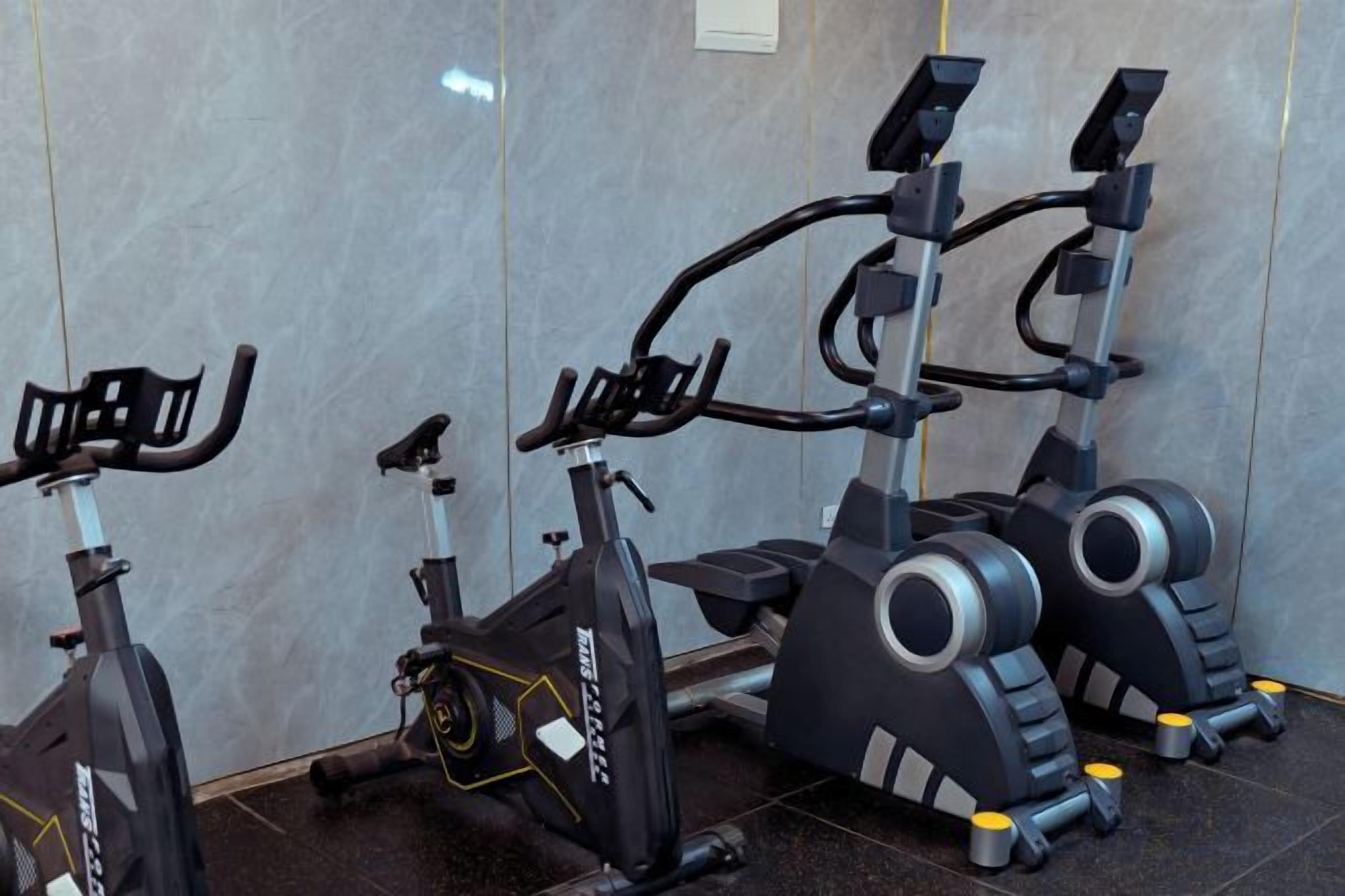 Tres bicicletas estáticas en un gimnasio con piso de baldosas y una pared lisa.