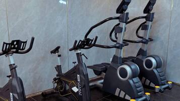 Tres bicicletas estáticas en un gimnasio con piso de baldosas y una pared lisa.