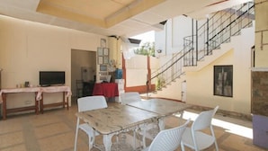 A dining area with a marble table and white chairs, a television, and a staircase leading to an upper level. - RedDoorz @ Yssa Ademar near Robinsons Jaro (Iloilo City)