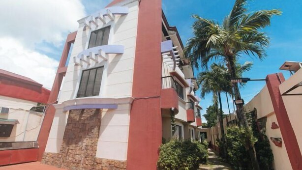 A modern building with a stone base and white upper levels, surrounded by palm trees and a clear sky. - RedDoorz @ Yssa Ademar near Robinsons Jaro (Iloilo City)