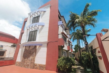 A modern building with a stone base and white upper levels, surrounded by palm trees and a clear sky.