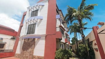 A building with a white facade and red accents, a palm tree, and a clear sky.