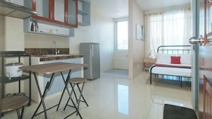 A compact kitchen with a dining table, chairs, a refrigerator, and a bed with a window view. - RedDoorz @ Yssa Ademar near Robinsons Jaro (Iloilo City)