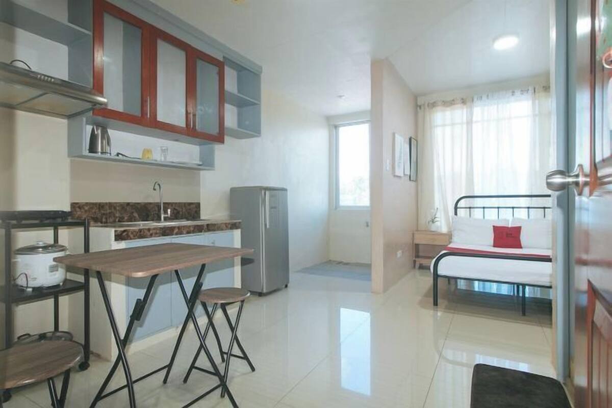 A compact kitchen with a dining table, chairs, a refrigerator, and a bed with a window view.