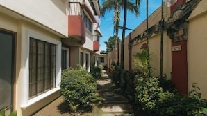 A narrow pathway flanked by buildings with balconies, surrounded by lush greenery and palm trees. - RedDoorz @ Yssa Ademar near Robinsons Jaro (Iloilo City)