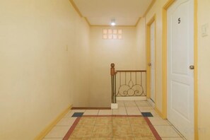 A hallway with a tiled floor, a wooden handrail, a white door with a number, and a small window. - RedDoorz @ Yssa Ademar near Robinsons Jaro (Iloilo City)
