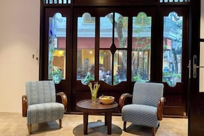 A room with two patterned chairs around a small round table, a decorative door with a view of the outside, and a small vase on the table.