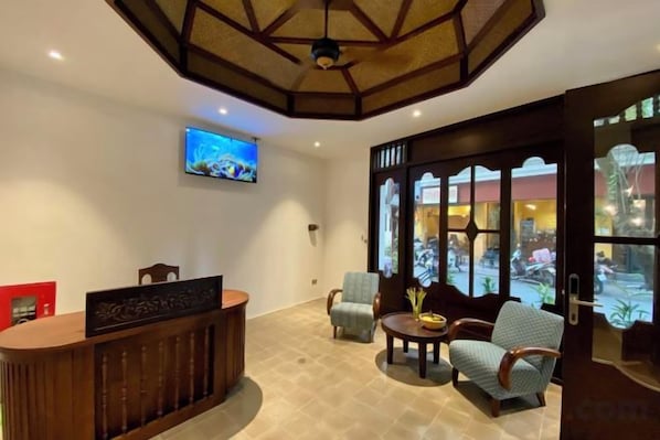 A reception area with a wooden reception desk, a television mounted on the wall, and seating arrangements including a chair and a sofa.