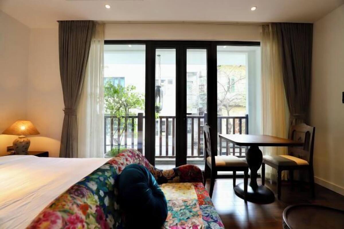 Habitación de hotel con cama, sofá, mesa de comedor con sillas y vista al exterior a través de una puerta corrediza.