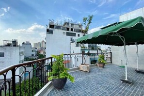 A rooftop terrace with a green awning, potted plants, and a metal railing.