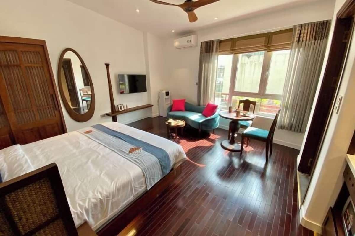 Habitación de hotel con cama, zona de estar con mesa y sillas, un espejo grande y una ventana con cortinas.