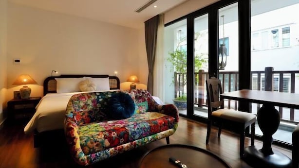 Een hotelkamer met een bed, een kleurrijke bank, een eettafel en uitzicht op het buiten.