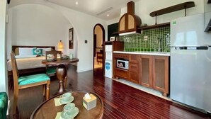 Een hotelkamer met een eettafel, stoelen, een bed en een kitchenette voorzien van een koelkast en een magnetron.