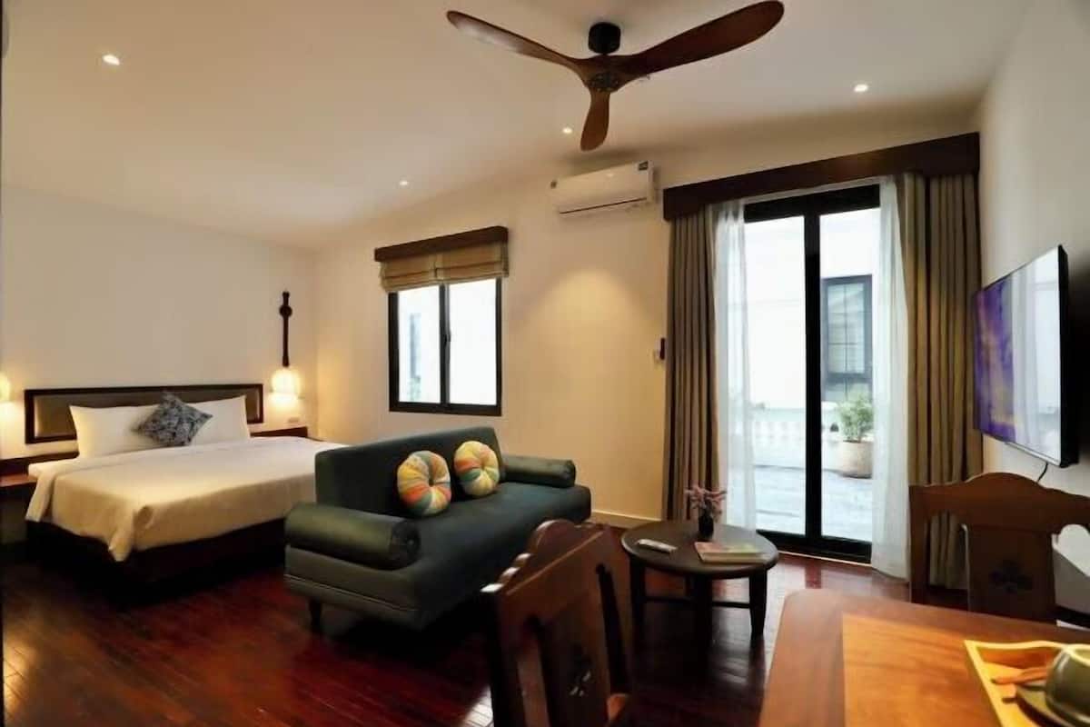 Habitación de hotel con cama, sofá, mesa de comedor, ventilador de techo y televisor.