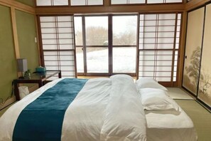 A room with a bed, a window with sliding shoji screens, a painting on the wall, and a small table with a lamp. - FujiAlpes (Fujikawaguchiko)