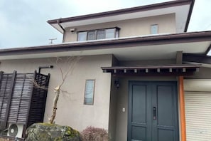 A modern two-story house with a dark blue door, a small balcony, and a stone feature in the front yard. - FujiAlpes (Fujikawaguchiko)