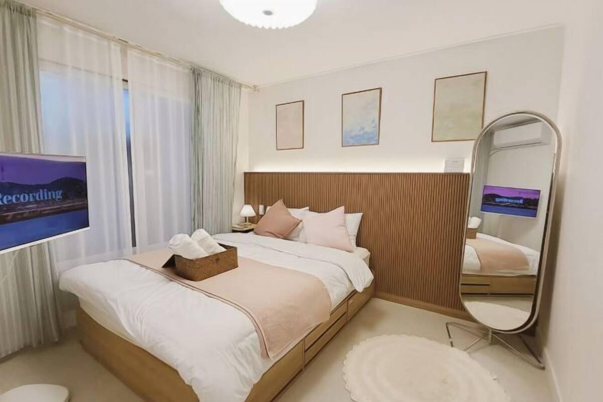 A modern hotel room with a large bed, a flat-screen TV, a bedside table, and a mirror.