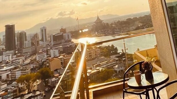 A balcony with a glass railing overlooking a cityscape, including buildings and a river. - Kuching City Center Riverine Apartment With Balcony & City Views (Kuching)