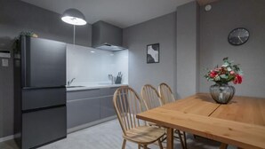A modern kitchen with a built-in refrigerator, a wooden dining table with four chairs, a vase with flowers, and a clock on the wall. - Travel Time・Pink Beach - Plum Luxury house: 33 min to KIX, 25 min to ITM,parking (Osaka)