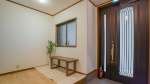 A room with a wooden floor, a bench, a potted plant, a door with a metal gate, and a fire extinguisher. - Travel Time・Pink Beach - Plum Luxury house: 33 min to KIX, 25 min to ITM,parking (Osaka)