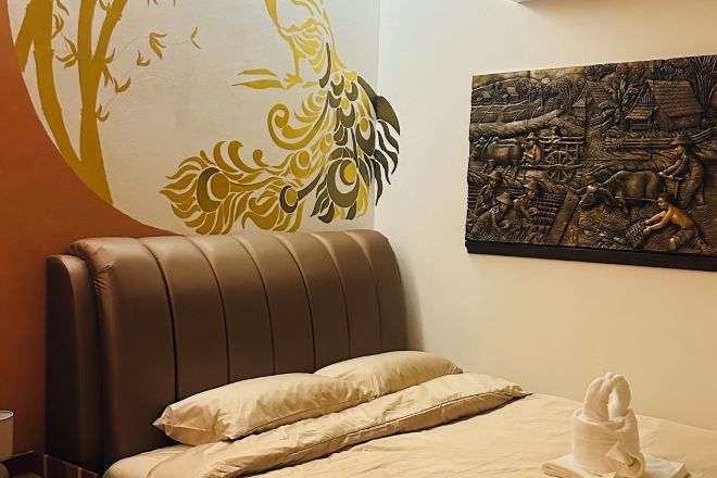 A hotel room with a brown leather headboard, a bed with beige bedding, a wall mural, and a towel sculpture on the bed.