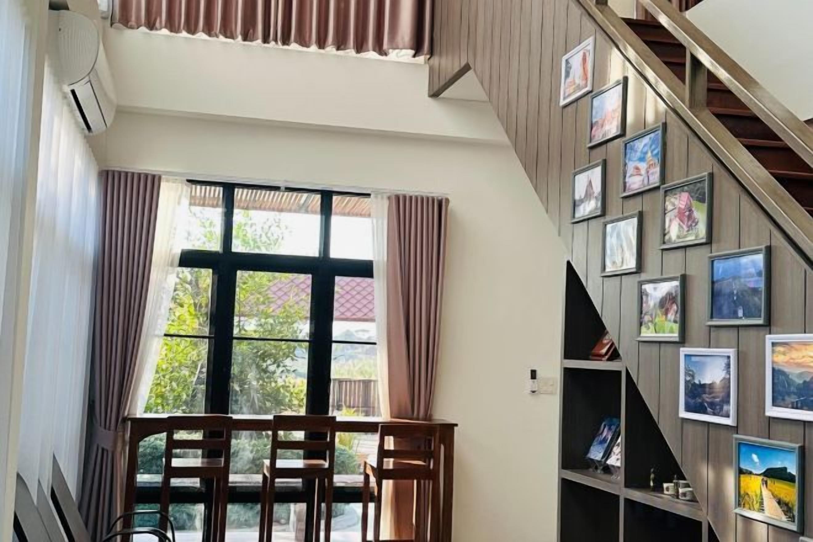 A room with a staircase, a dining area with chairs, and a wall with framed pictures.