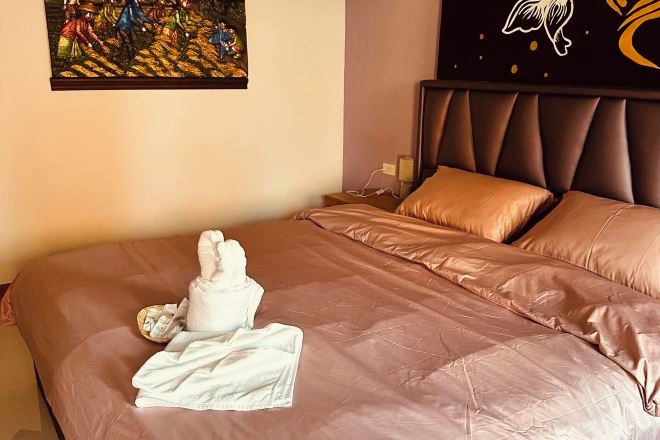 A neatly made bed with a brown cover, a white towel, and a white robe on it.