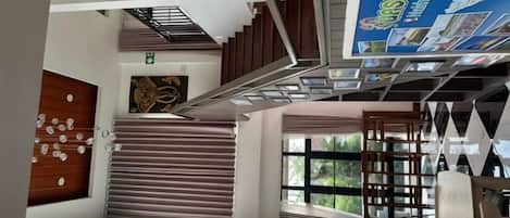 Interior moderno de hotel con una escalera, una zona de estar y un ventanal grande.