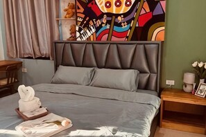 Une chambre à coucher avec un lit gris, une tête de lit, une table de chevet et une tapisserie colorée au mur.
