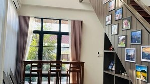 Una stanza con un tavolo da pranzo e sedie, una scala con quadri incorniciati e un'ampia finestra con tende.