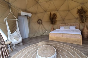 Een tent met een bed, een hangstoel en geweven vloermatten.